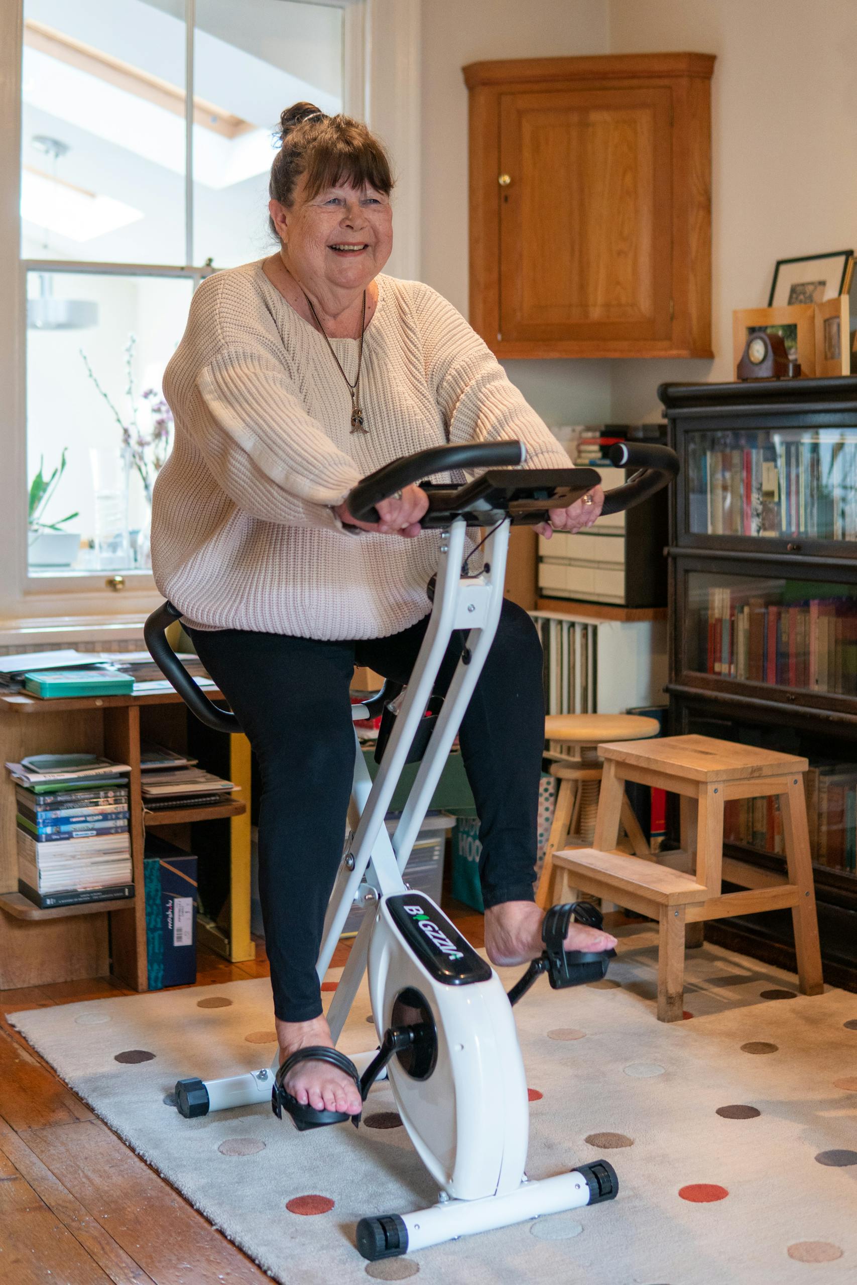 Smiling woman exercises on stationary bike in cozy home setting. Indoor fitness and lifestyle.